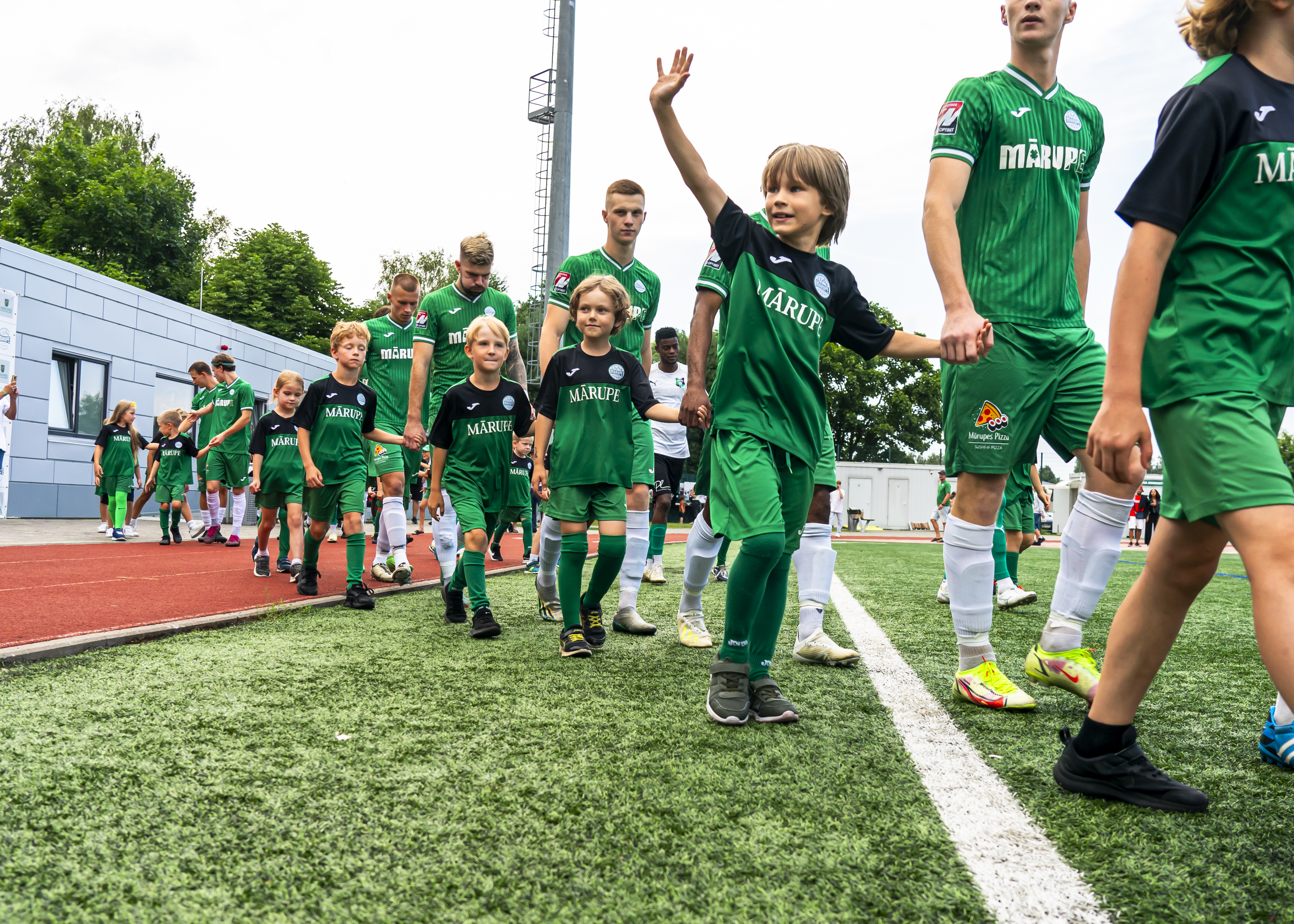 Bērni zaļos futbolistu tērpos pavada uz spēles laukuma lielos futbolistus