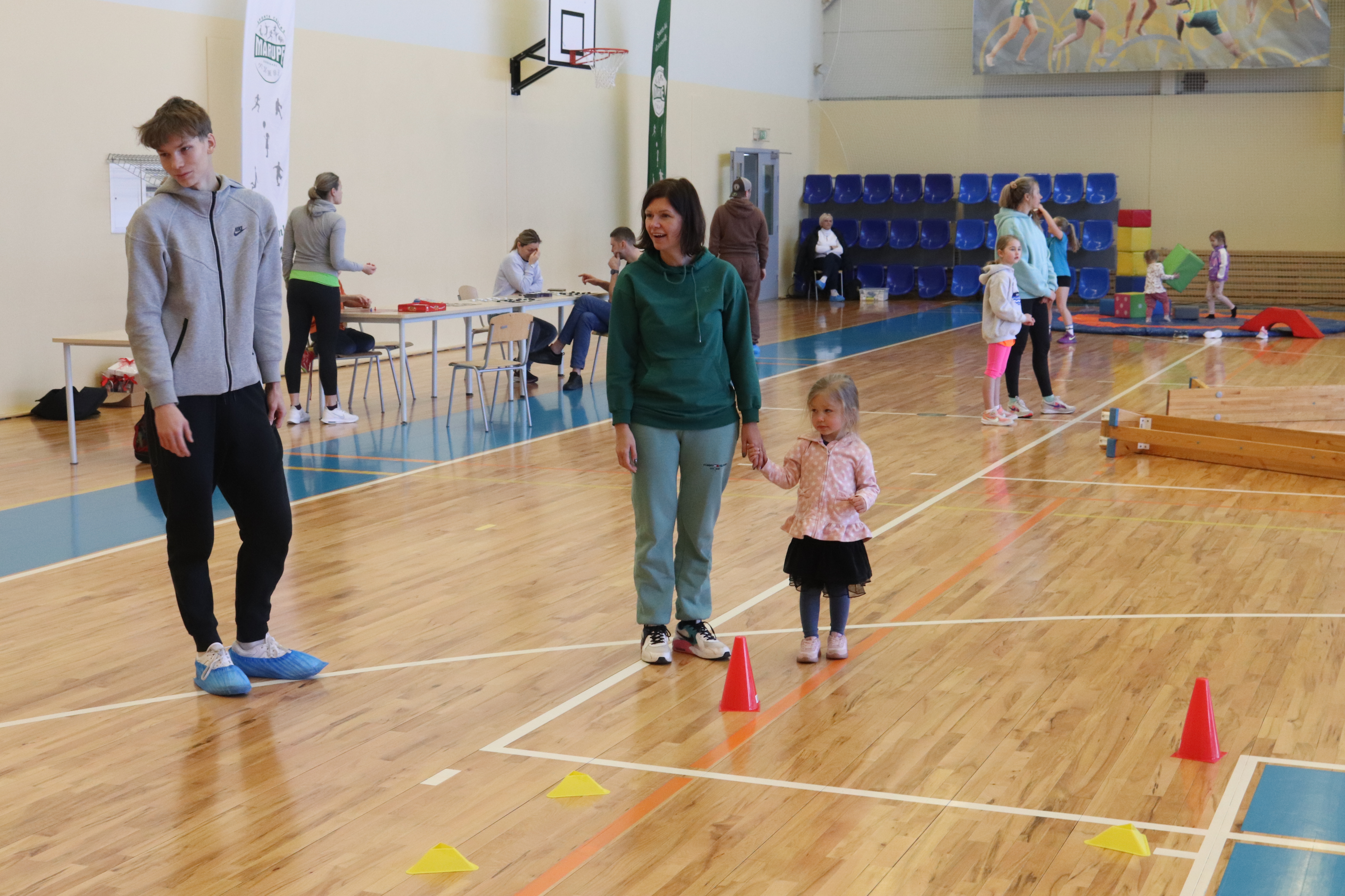 Sieviete ar mazu meitenīti un jaunieti stāv sporta zālē