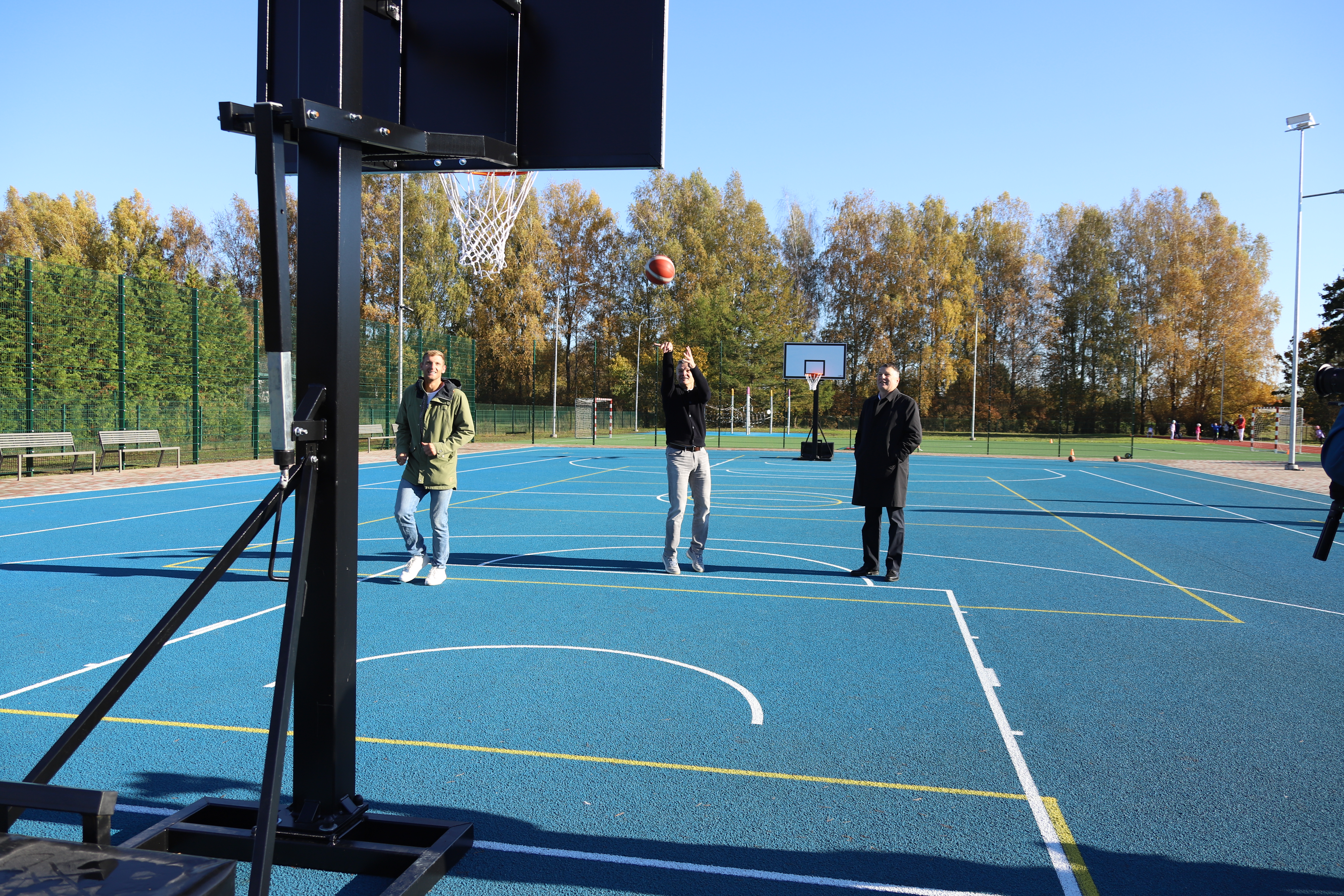 trīs vīrieši basketbola laukumā, viens no viņiem met bumbu