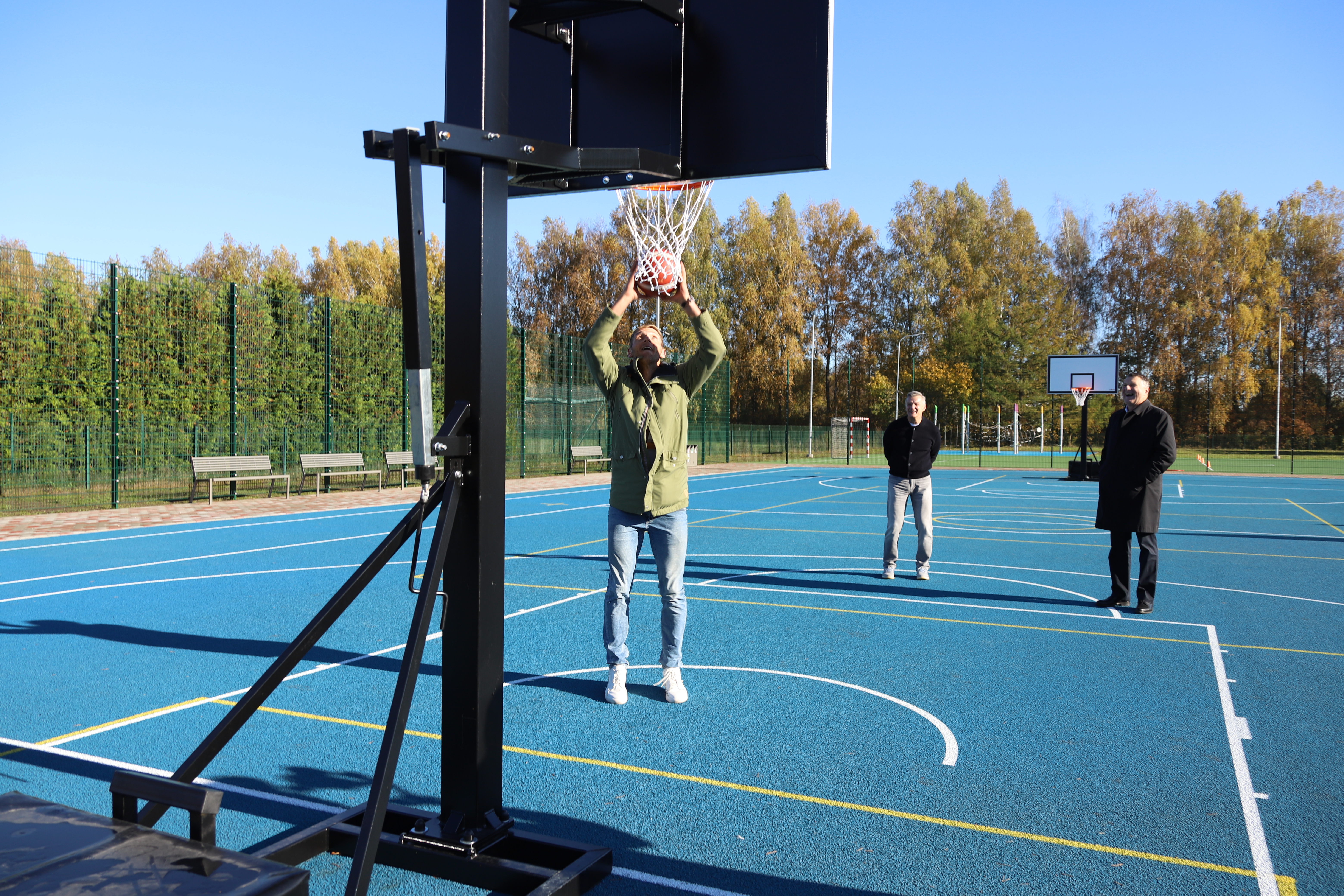 vīrietis zaļā jakā met bumbu basketbola grozā