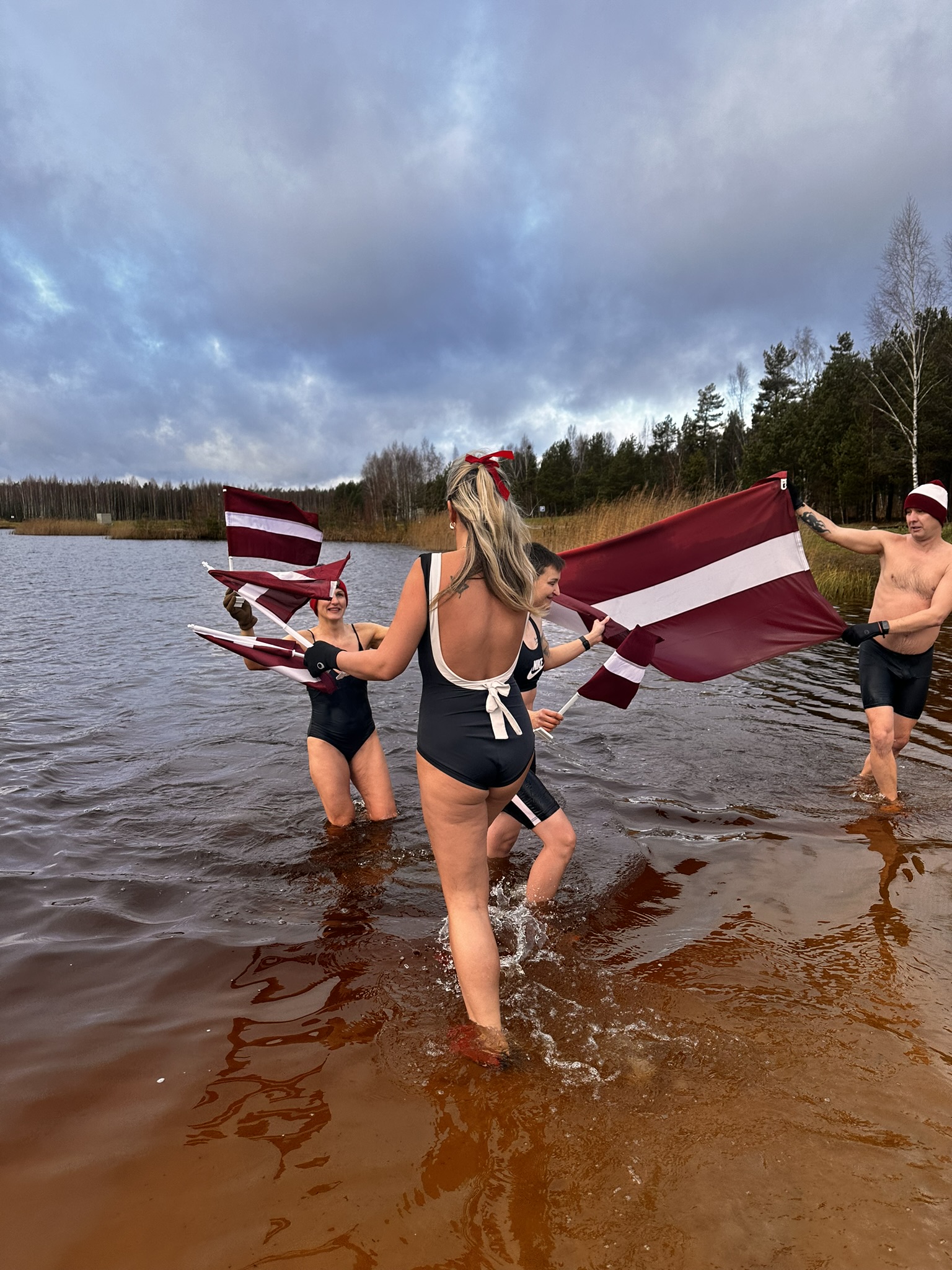 Cilvēki ūdenstilpnē nes Latvijas karogu