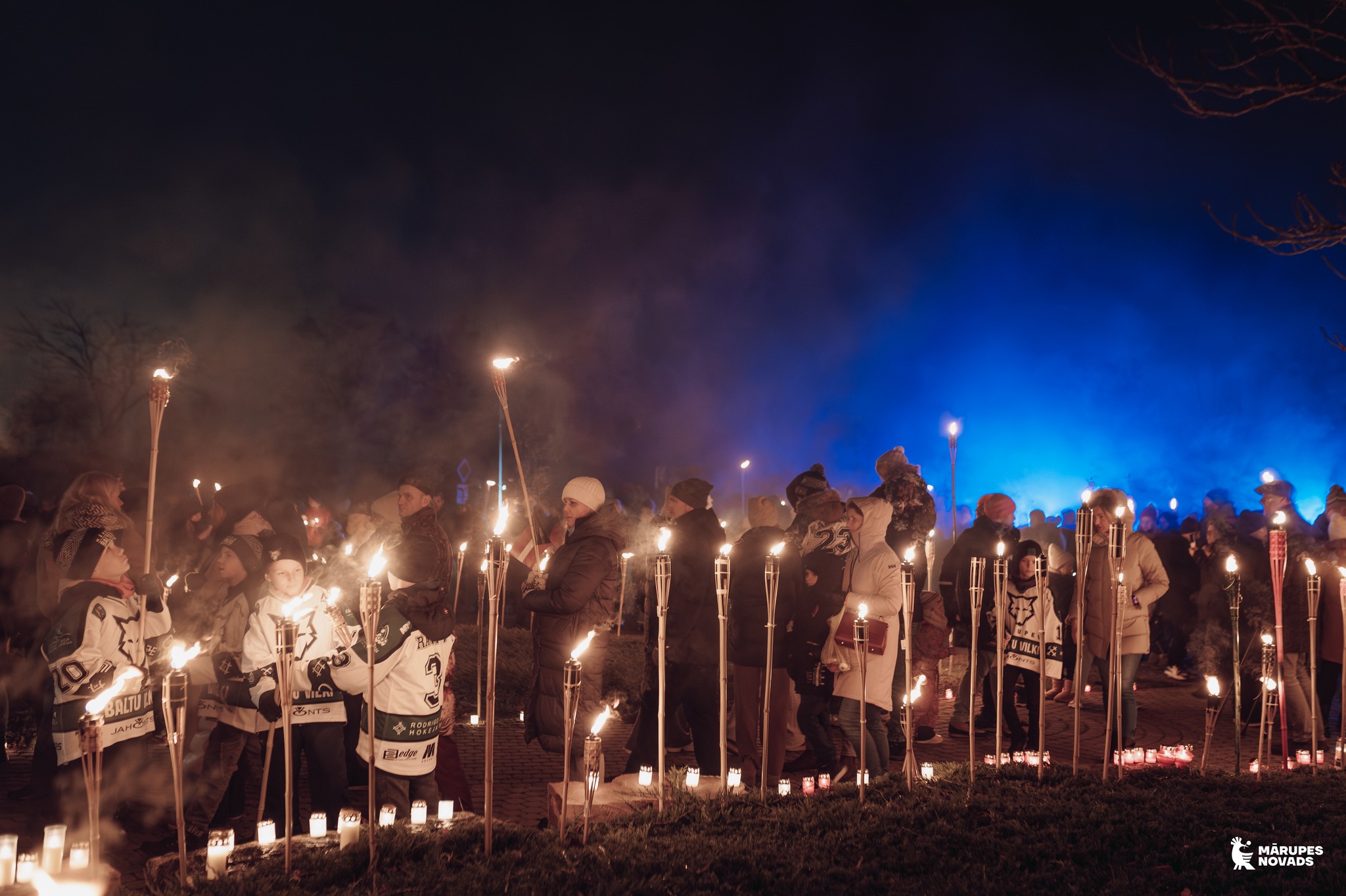 Cilvēki ar lāpām rokās dodās lāpu gājienā tumšā vakarā