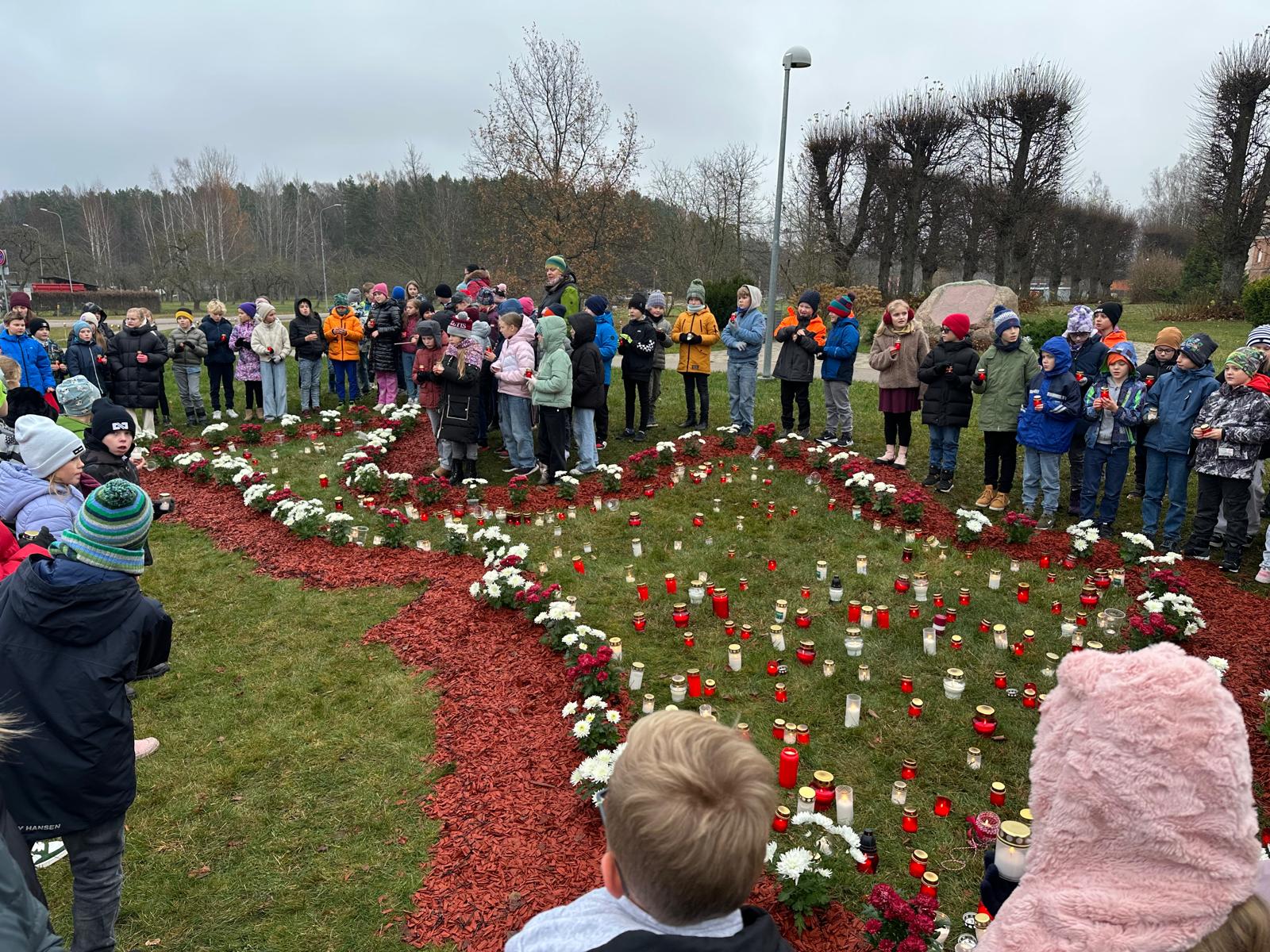 Bērni ar svecītēm rokās pie pļavā veidotas Latvijas kontūras