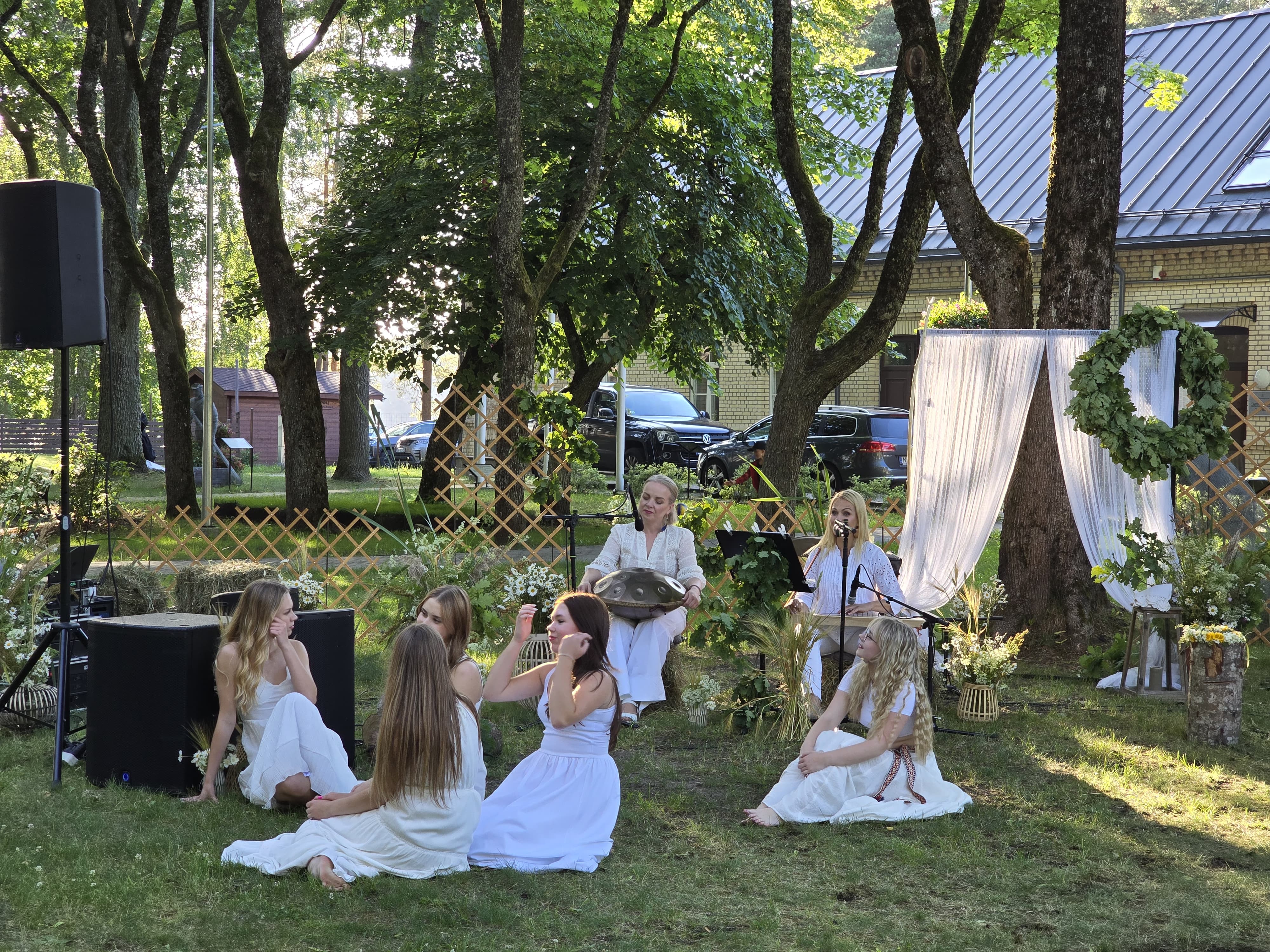 Popgrupas dalībnieki baltos kostīmos dzied un dejo saulainā vasaras vakarā brīvdabā