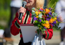 Sieviete ar ziediem rokās runā mikrofonā
