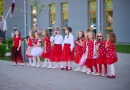 Bērnu popgrupa sarkanos tērpos dzied āra laukumā