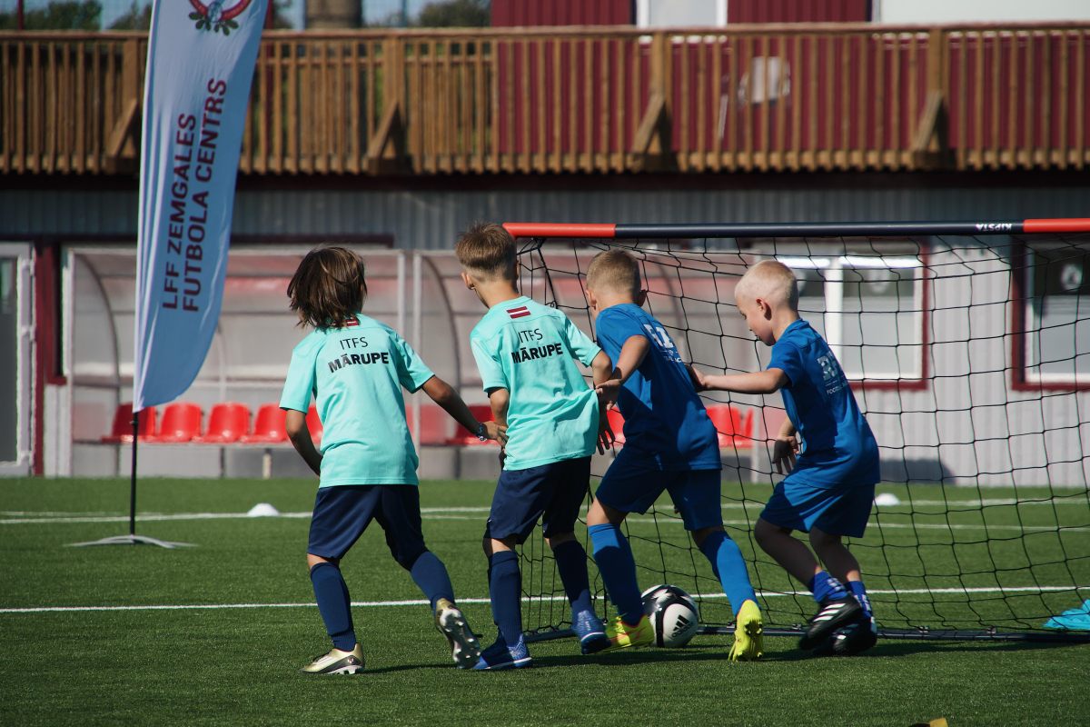 Bērni zilos kreklos skrien pa futbola laukumu