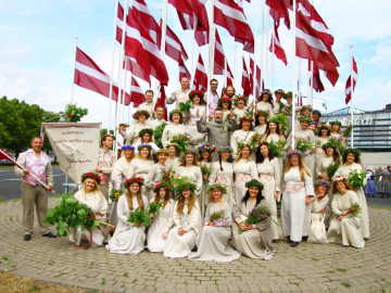 Koris gaišos tērpos pie Latvijas karogiem