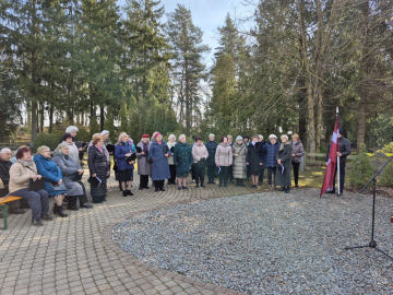 Sieviešu koris stāv un dzied brīvdabā piemiņas pasākumā