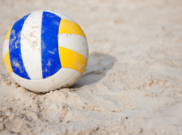 Volejbola laukuma smiltis un bumba ar zilām un dzeltenām krāsām