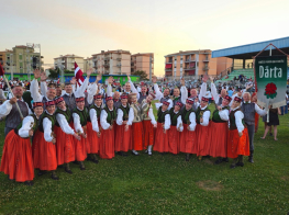 Deju kolektīva dalībnieki balti sarkanos tērpos ar karogiem stadionā pēc festivāla gājien