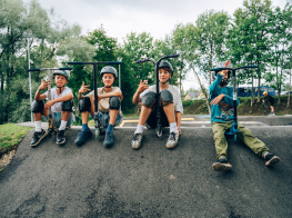 Četri bērni ar skūteriem sēž pump track trasē