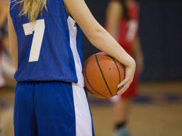 meitene zilā kreklā tur rokā basketbola bumbu