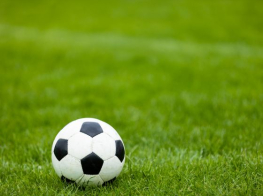 Futbola bumba ar melniem rombiem stāv zaļā zālē