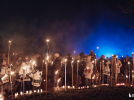 Cilvēki ar lāpām rokās dodās lāpu gājienā tumšā vakarā