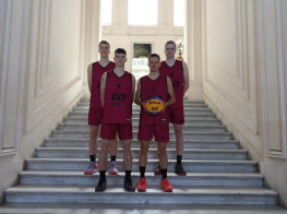 Četri puiši sarkanos sporta tērpos stāv uz baltām trepēm, vienam no puišiem rokās basketbola bumba