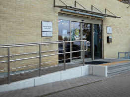 ķieģeļu ēka ar elektriskajām durvīm un pelēku plāksni pie sienas