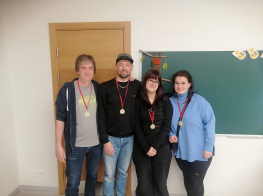 Divi vīrieši un divas sievietes stāv klasē pie tāfeles