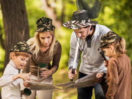 Divi bērni kopā ar vecākiem mežā skatās teritorijas kartē