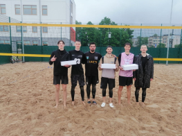 Vīrieši sporta tērpos stāv pludmales volejbola laukumā